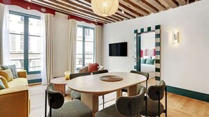 Una habitación de hotel moderna con techo de madera, una mesa de comedor redonda, asientos cómodos, un televisor de pantalla plana y un espejo grande.