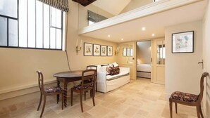 A dining area with a table and chairs, a sofa, and a window with curtains. - A Charming 2-BR/2Ba in Saint Germain (Paris)