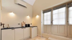 A kitchen with a black countertop, white cabinets, and a built-in oven. There are two windows with checkered curtains. - A Charming 2-BR/2Ba in Saint Germain (Paris)