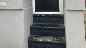 Une porte d’entrée noire avec une petite fenêtre, une poignée en métal et une fente pour le courrier.