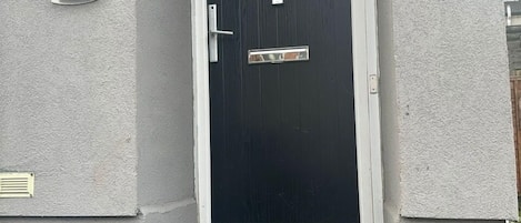 Una puerta frontal negra con un ventanal pequeño, un picaporte de metal y un buzón.