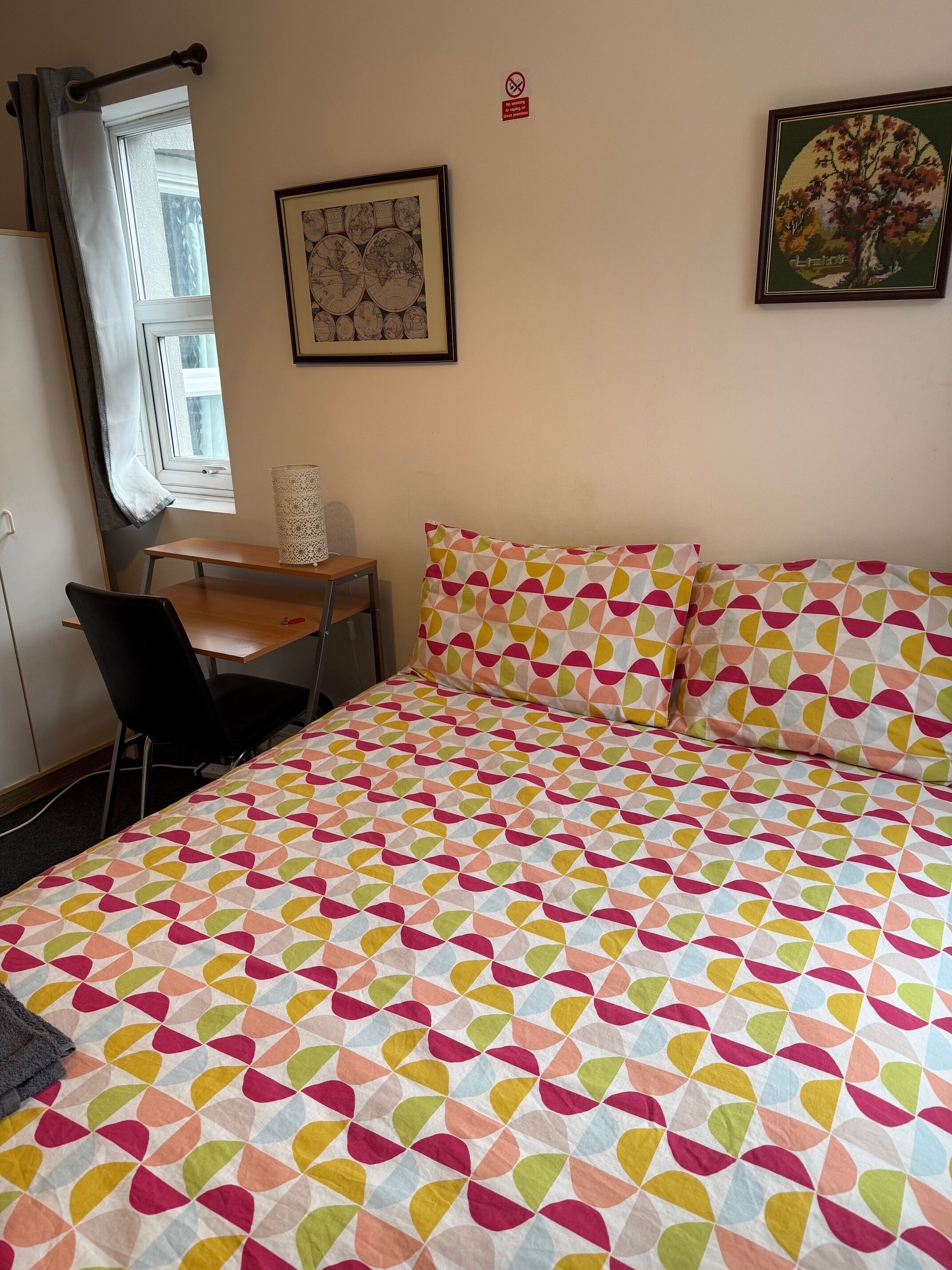 Un dormitorio con cama, escritorio, silla y ventana con cortinas.