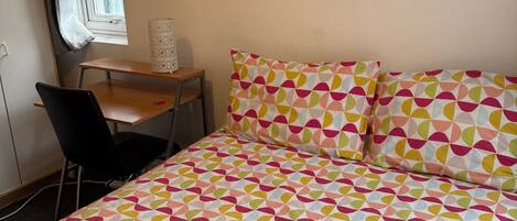 A bedroom with a bed, a desk, a chair, and a window with curtains.