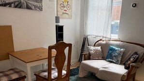A cozy living room with a wooden table and chairs, a sofa with patterned cushions, and a large rug. - Luton Homestay near AIRPORT  (Luton)