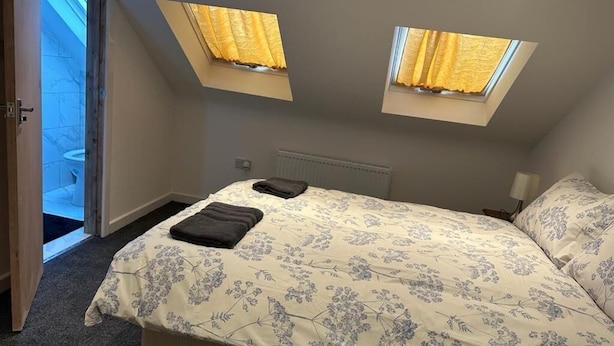 A bedroom with a bed, two windows, and a door leading to a bathroom. - Luton Homestay near AIRPORT  (Luton)