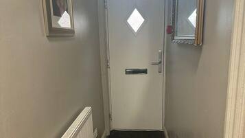 A narrow hallway with a white door, a radiator, a doormat, and a framed picture on the wall.