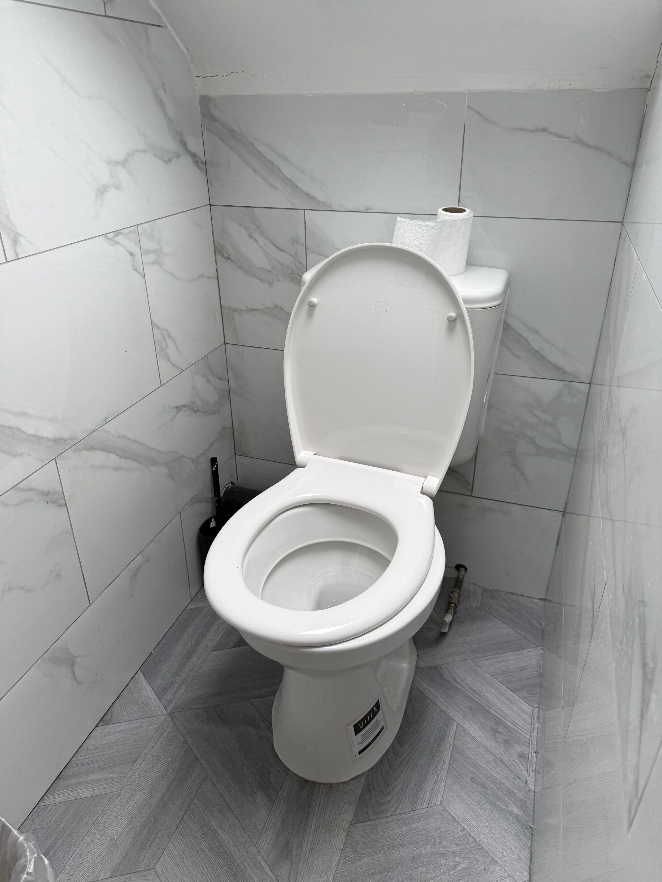 A toilet in a bathroom with marble tiles on the walls and floor.