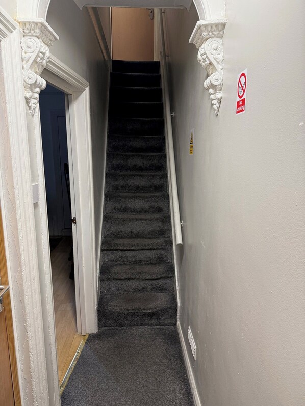 A staircase with a carpeted landing and a no-smoking sign on the wall. - Luton Homestay near AIRPORT  (Luton)