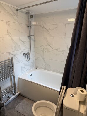 A bathroom with a bathtub, toilet, shower, and a towel rack. - Luton Homestay near AIRPORT  (Luton)