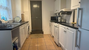 A compact kitchen with white cabinets, a microwave, a stove, and a refrigerator. - Luton Homestay near AIRPORT  (Luton)