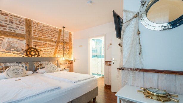 Un dormitorio con cama, cabecero de madera, decoración con timón de barco, televisión y ventana.