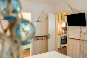 Ein Zimmer mit einem Bett, einer Holztür, einer Küchenzeile und einem an der Wand montierten Fernseher.