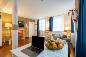 Ein modernes Wohnzimmer mit Laptop auf einem Tisch, Kamin, Sofa und einem Essbereich mit Lampe.