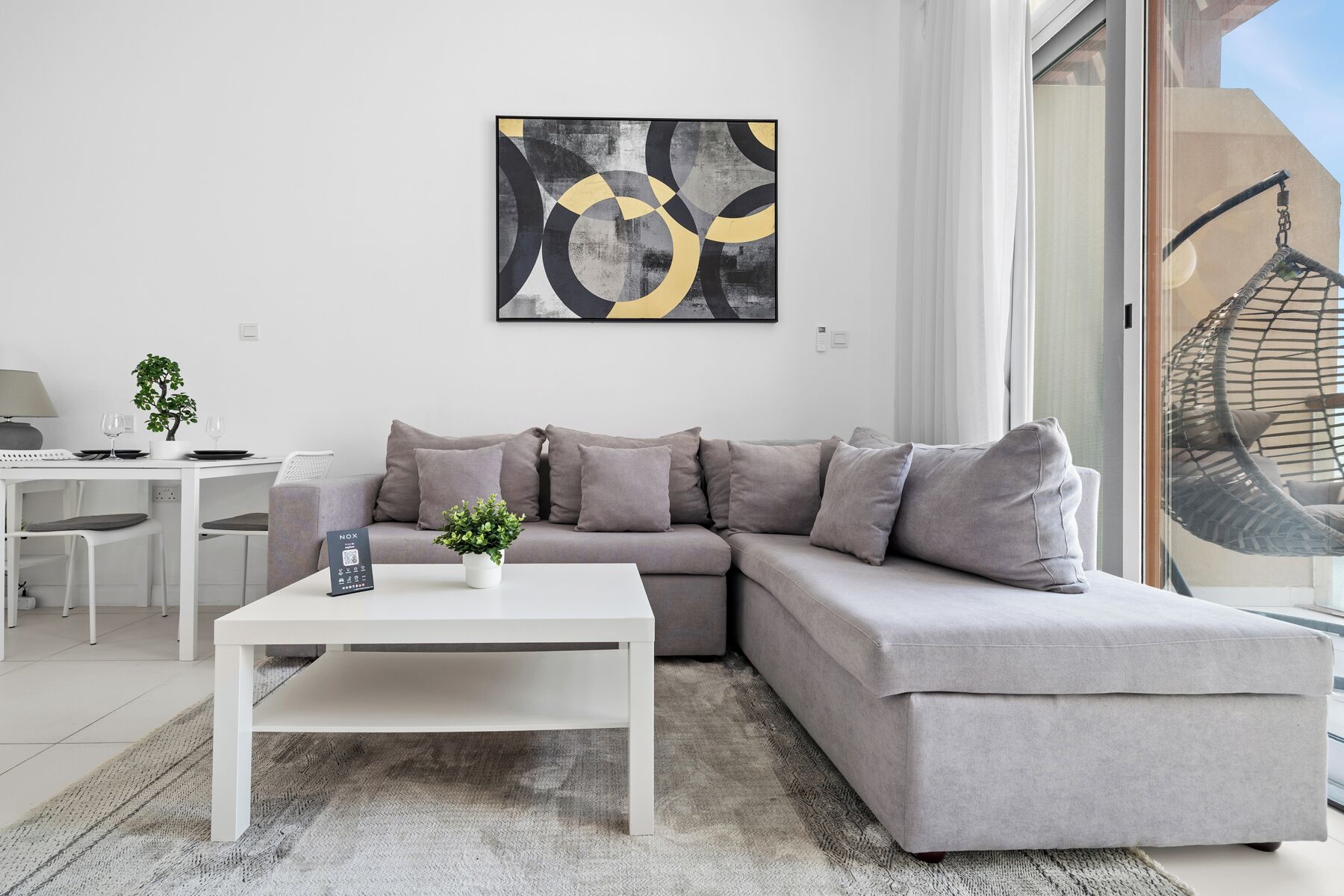 A modern living room with a grey sectional sofa, a white coffee table, and a minimalist abstract painting on the wall.