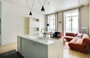A modern kitchen with a central island, a dining area with a table and chairs, and a living area with a sofa and a TV. - A Bright 1-BR in Grands Boulevards (Paris)