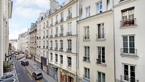 A row of multi-story buildings with balconies, a street with parked cars, and storefronts including a visible 'CARLA' sign. - A Bright 1-BR in Grands Boulevards (Paris)