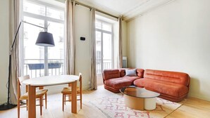 A living room with a red sofa, a round coffee table, a dining table with chairs, and a floor lamp. - A Bright 1-BR in Grands Boulevards (Paris)
