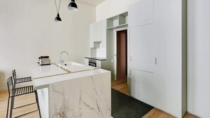 A modern kitchen with a marble island, black pendant lights, and a view into the adjacent living area. - A Bright 1-BR in Grands Boulevards (Paris)