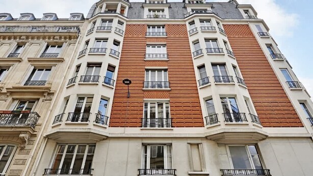 Un immeuble à étages, de style architectural classique, caractérisé par un panneau central en bois, de nombreux balcons et une façade symétrique.