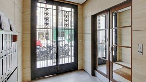 Un couloir avec une grande porte noire ornée de barreaux en métal décoratifs, un sol carrelé et un mur en bois.