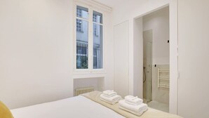 Une chambre d’hôtel avec un lit, une fenêtre, un radiateur et une porte donnant sur une salle de bain.