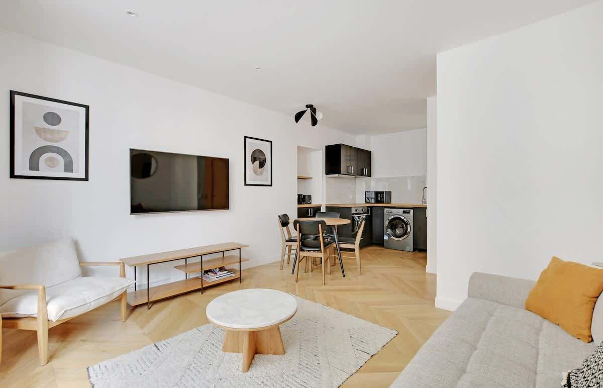 A modern living room with a sofa, a round coffee table, and a dining area with chairs.