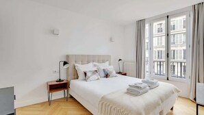 Ein Schlafzimmer mit einem großen Bett, Nachttischen, einem Heizkörper und einem Fenster mit Vorhängen.