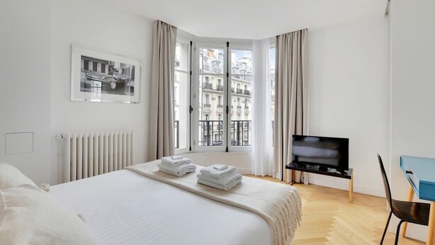 Ein Hotelzimmer mit Bett, Fernseher, Schreibtisch und einem Fenster mit Vorhängen.