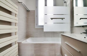 A modern bathroom with a bathtub, a large mirror, and a window. - A Stunning 1-BR in Saint Michel Notre Dame (Paris)