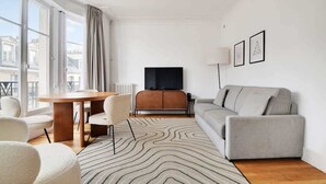 Ein modernes Wohnzimmer mit einer Couch, einem Esstisch mit Stühlen, einem Flachbildfernseher und einer Heizung.