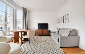 A modern living room with a sofa, a dining table with chairs, a flat-screen TV, and a radiator. - A Stunning 1-BR in Saint Michel Notre Dame (Paris)