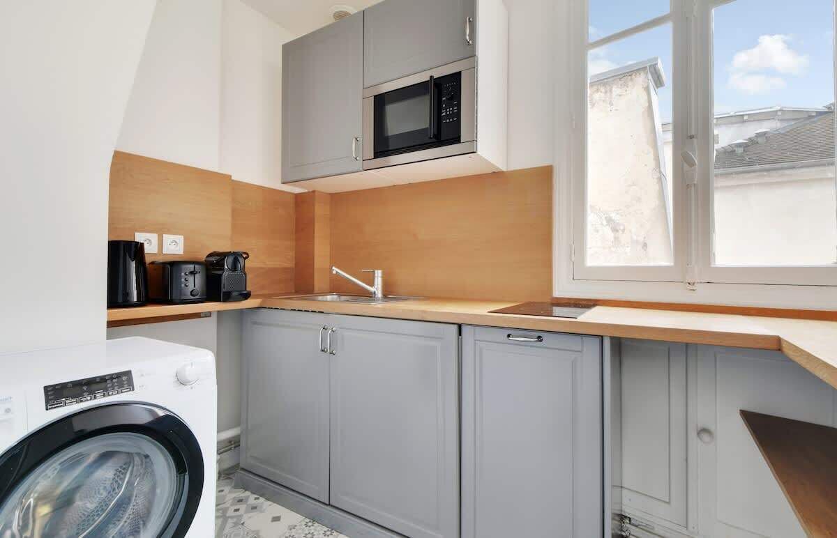 A compact kitchen with grey cabinets, a microwave, a sink, and a washing machine.