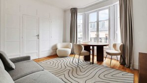 Ein modernes Wohnzimmer mit einem grauen Sofa, zwei Sesseln, einem runden Tisch und einem gemusterten Teppich.