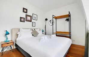Una habitación de hotel moderna con una cama grande, una mesita de noche con lámpara y una estructura de literas.