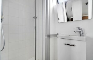 Un baño moderno con cabina de ducha de vidrio, un lavabo blanco con grifo cromado y un espejo sobre el lavabo.