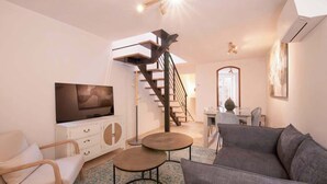 Un salon moderne avec un escalier, un téléviseur à écran plat, un canapé et un coin repas.