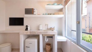 Eine kompakte Küchenzeile mit Mikrowelle, Toaster und Spüle. Es gibt einen kleinen Kühlschrank, einen Korb und ein Fenster mit Blick nach außen.