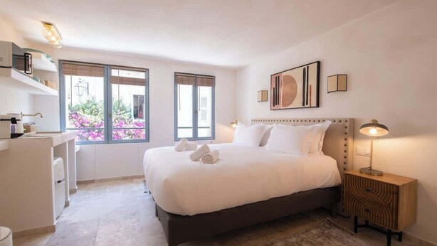 Ein Schlafzimmer mit einem großen Bett, Nachttischen, einem Schreibtisch und einem Fenster mit Blick auf Blumen.