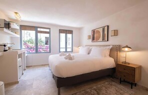 A bedroom with a large bed, bedside tables, a desk, and a window with a view of flowers. - A Magnificient Studio - Heart of Saint-Tropez (Saint-Tropez)