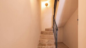 Un escalier muni d’une rampe, menant à un palier où est fixée une applique murale.