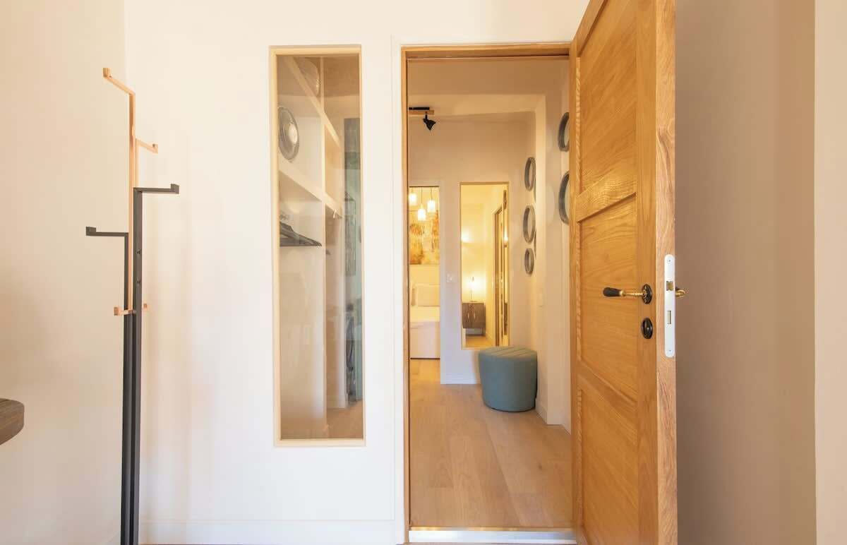 Un pasillo con una puerta de madera, un perchero y una división de vidrio.