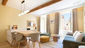 Un salon moderne avec un plafond en bois, un coin repas comprenant des chaises et une table, un canapé et une vue sur les bâtiments à travers de grandes fenêtres.