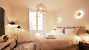 Hotelkamer met een groot bed, bedlampen, een nachtkastje, een raam met natuurlijk licht en een decoratieve hanglamp.
