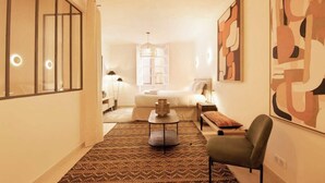 Een hotelkamer met een bed, een zithoek met een stoel en een tafel, een groot abstract schilderij aan de muur en een kamerbreed tapijt.