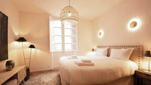 Une chambre d’hôtel avec un grand lit, des lampes de chevet, une télévision et une fenêtre laissant entrer la lumière naturelle.