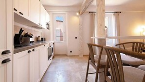 Een keuken met witte kasten, een fornuis en een spoelbak. Er staat een houten eettafel met stoelen.