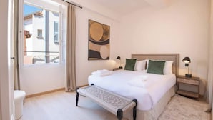 Een slaapkamer met een bed, nachtkastjes, een bankje, een raam en een schilderij.