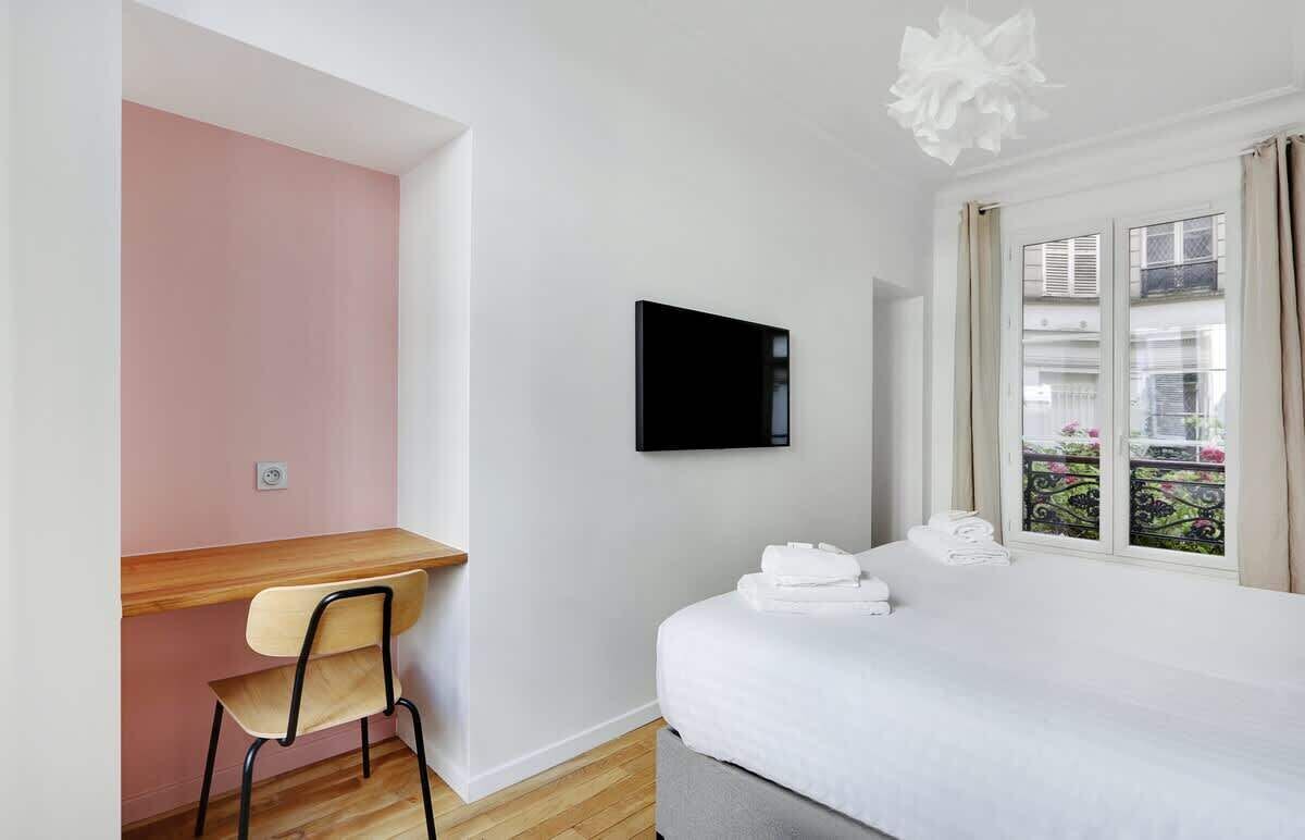 A hotel room with a bed, a desk, a chair, a television, and a window with curtains.