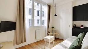 A modern living room with a large window, a flat-screen TV, a small round table, a white sofa, and a black cabinet. - A Pleasant Studio in La Madeleine-Opéra (Paris)