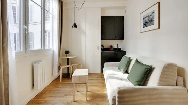 Ett modernt vardagsrum med en soffa, ett litet bord, en stol, ett element och ett fönster med gardiner.